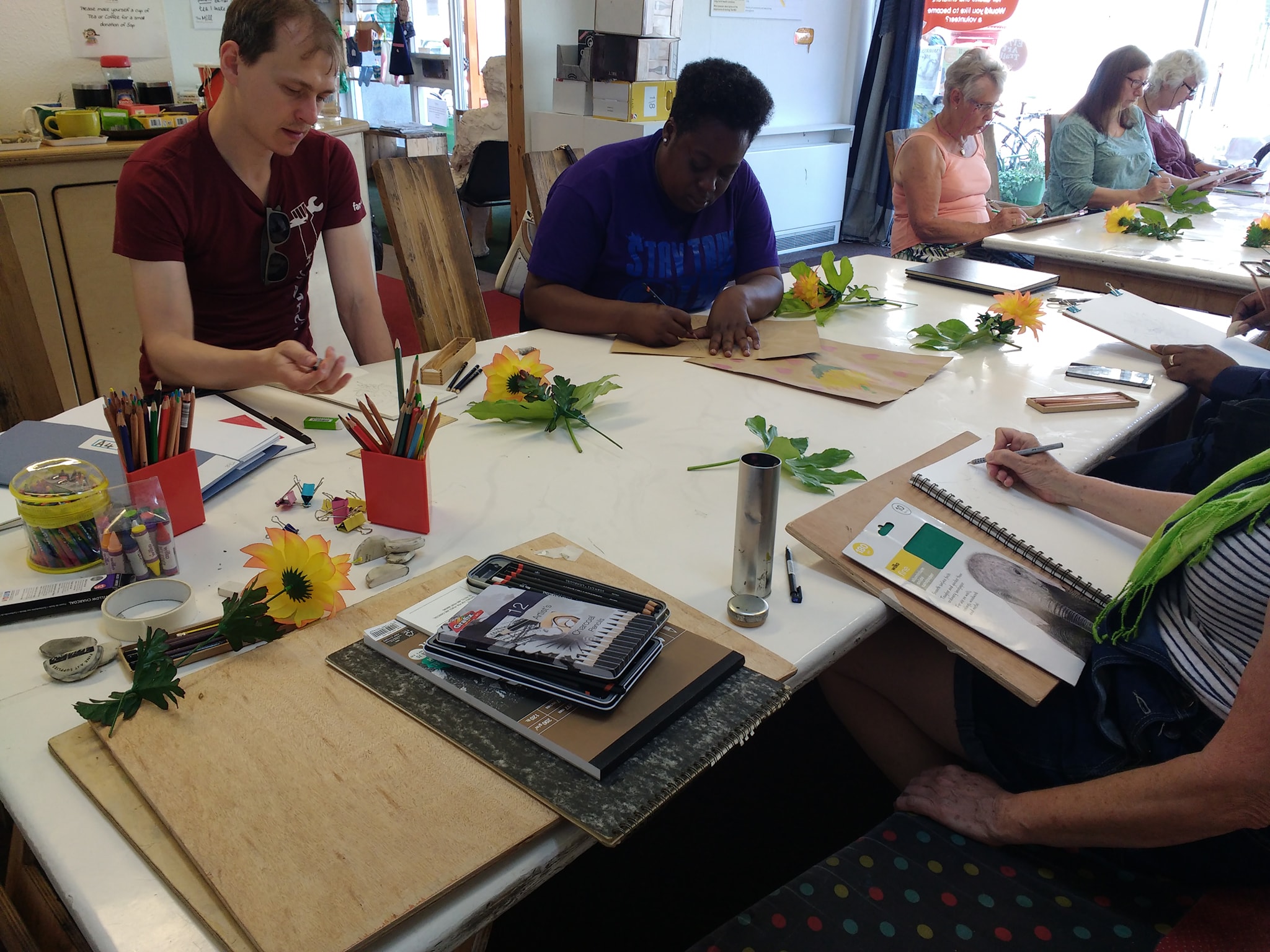 Group of people drawing still life flowers in the Mill living room, with art materials everywhere