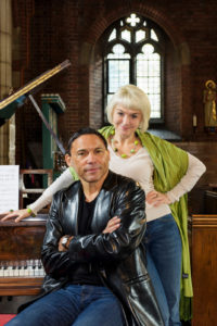 Gillian Keith and Tom Randle, sitting and standing next to a grand piano.