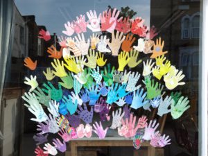 A window display of coloured hand prints of all sizes and different decoration, in a rainbow