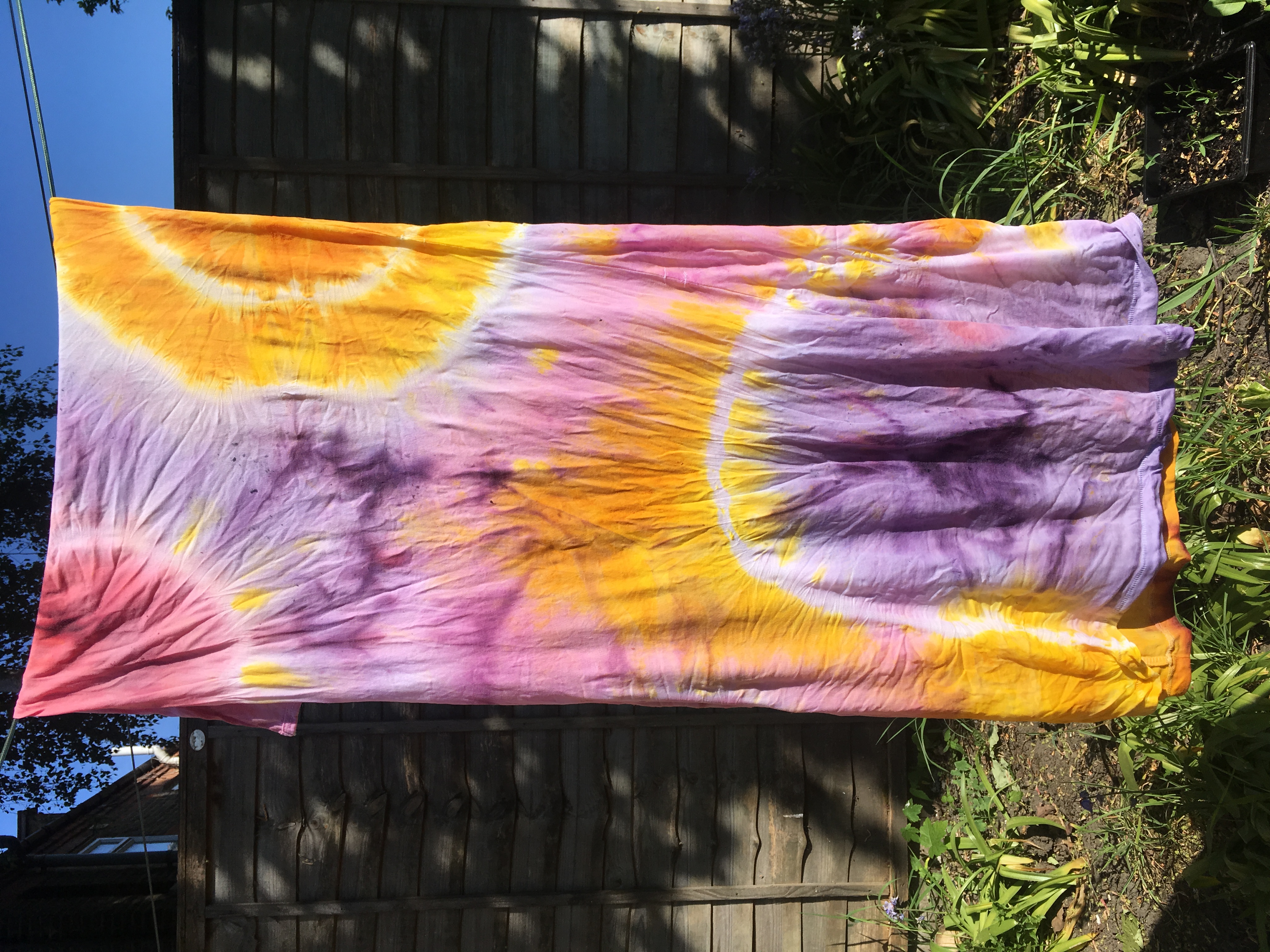 A tie-dyed cloth with swirling colours hanging to dry i nthe sun