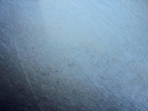 An extreme close-up photograph of ice cracking on a car window. As there is no sense of scale it appears to be a blue-grey landscape with fine dark cracks forming abstract shapes across the surface.