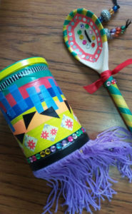 A colourful shaker made from a tin can and decorated with feathers, and a clacker made from a wooden spoon which has been painted with bright colours