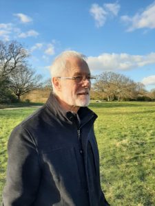Richard Bennett standing in an open field in the sunshine, with bare winter trees in the background. 