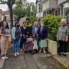 A group of people standing on the pavement outside a house, one of them is holding up the E17 Art Trail brochure, they're looking at the camera and seem to be having a good time together