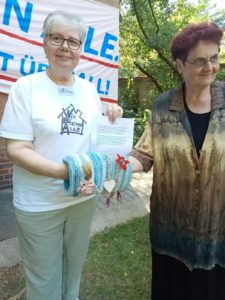Two people from Stille Strasse trying out a knitted twiddlecuff, a knitted tube fitted with ribbons and buttons, designed for people with dementia to use